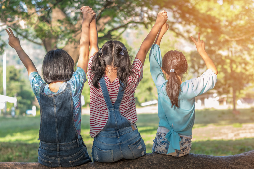 Backs of three girls, hands clasped above their, sunny day outside