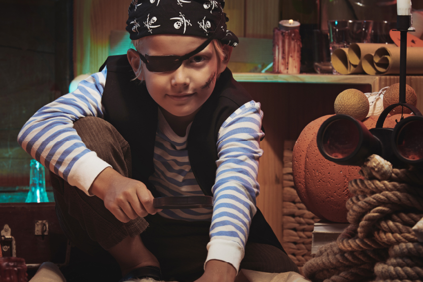 Young boy dressed as pirate, pointing at a treasure map, various ship-related details in background