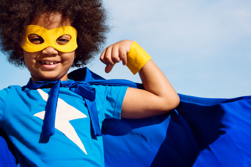 Young girl in superhero costume, flexing her bicep and smiling at camera