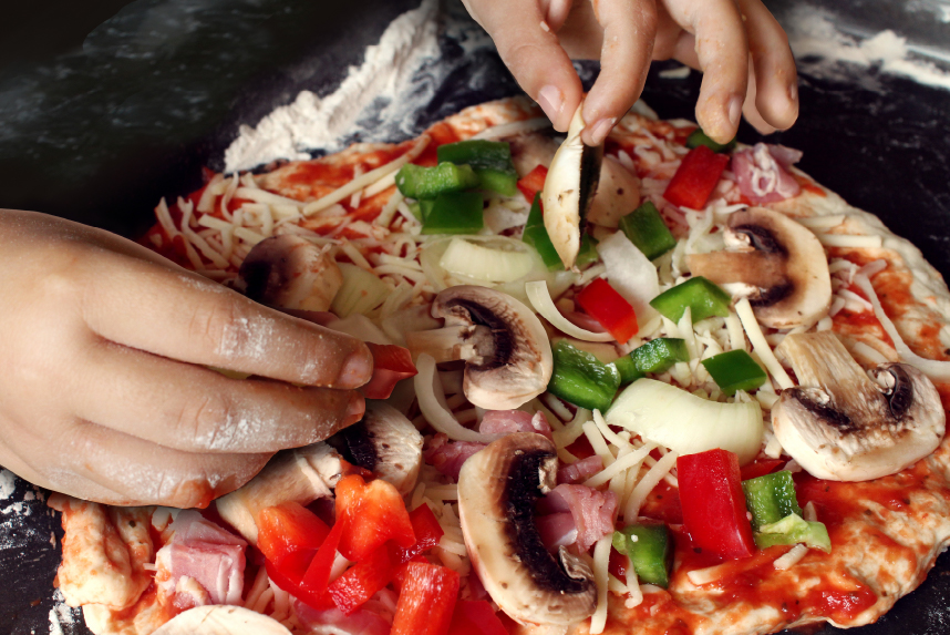 Child's hands putting toppings on pizza
