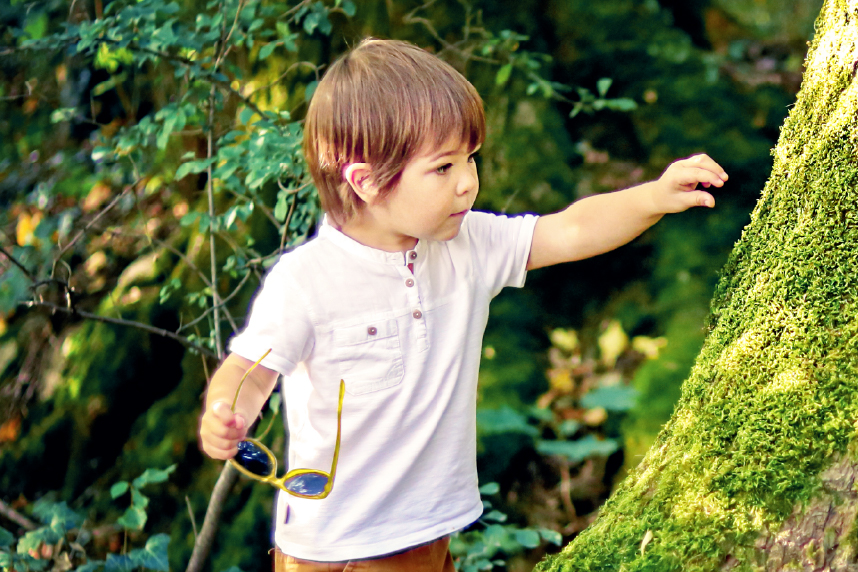 Young boy reaching out to touch a moss-covered tree