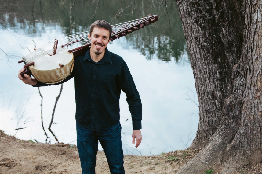 Sean Gaskell holding a kora in front of a body of water