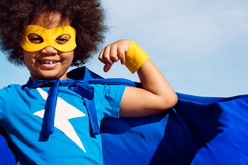 Young girl in superhero costume, flexing her bicep and smiling at camera