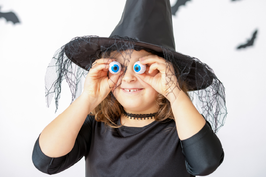 Girl dressed a witch and holding eyeball toys in front of her eyes