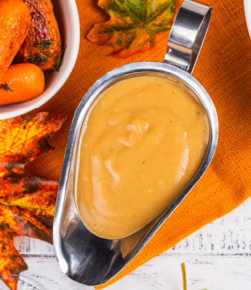 Overhead shot of a gravy boat filled with brown gravy on orange background