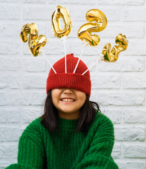 Girl with beanie pulled over her eyes and 2023 balloons stuck in the brim