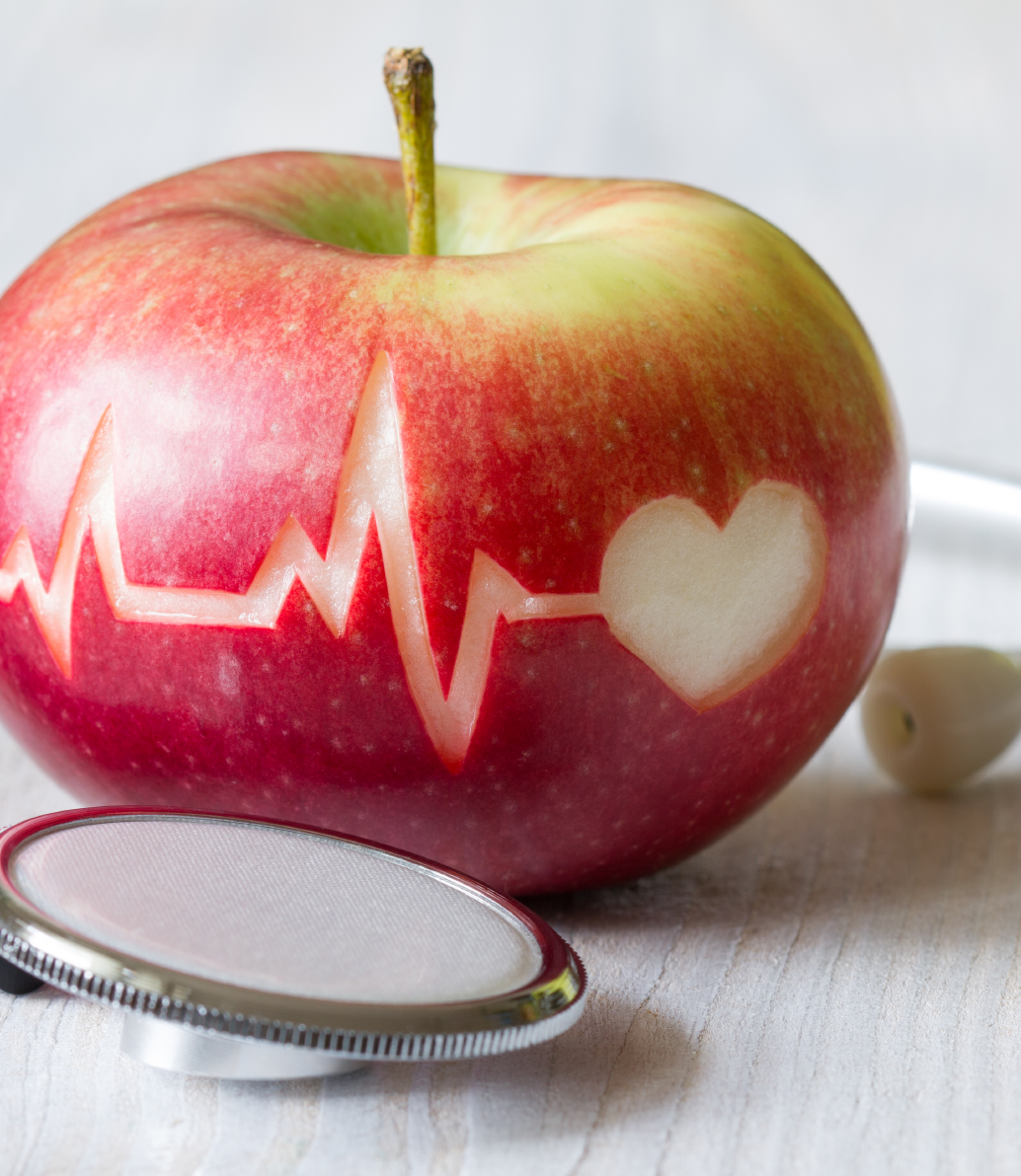 Stethoscope and apple; apple has monitor waves and a heart carved into its peel