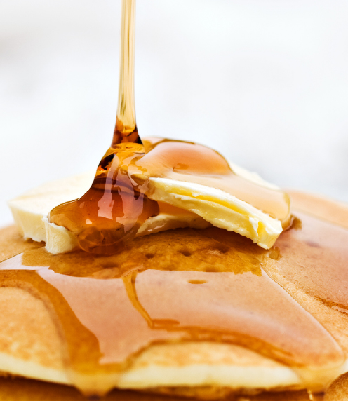Close up of maple syrup drizzling on butter and pancakes