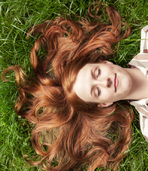 Teenager laying on the grass, eyes closed and hair fanned out around her