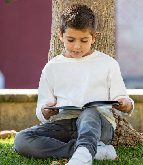 Boy reading book while leaned against a tree