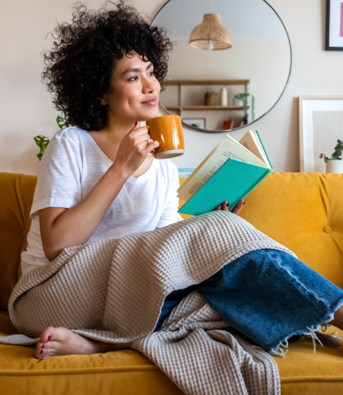Woman drinking from cup with book and blanket