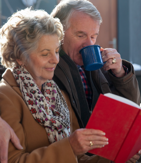 Senior couple sharing a book while the man drinks from a cup