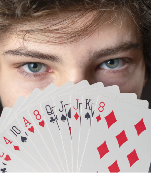 Teenage boy looking at viewer over a fan of playing cards