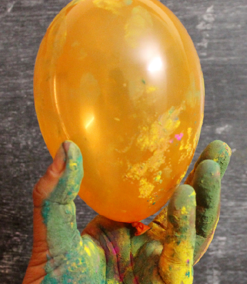 Paint-covered hand holding an orange balloon