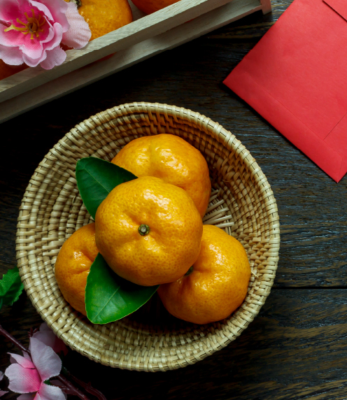 Wicker bowl of small oranges, a red envelope, and flowers