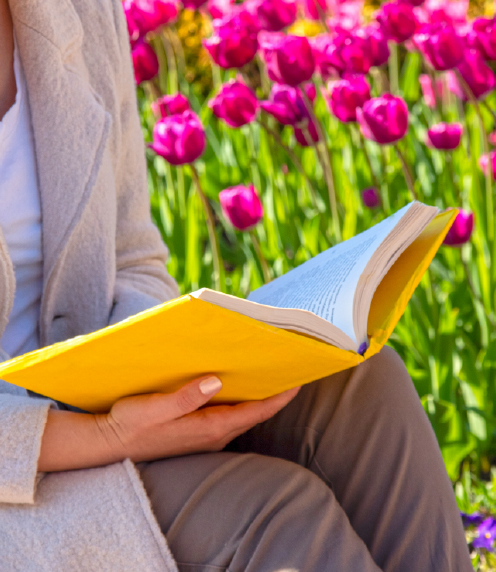 Woman reading book outside with pink flowers