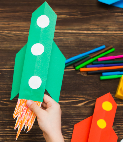 Child's hand holding green construction paper rocket