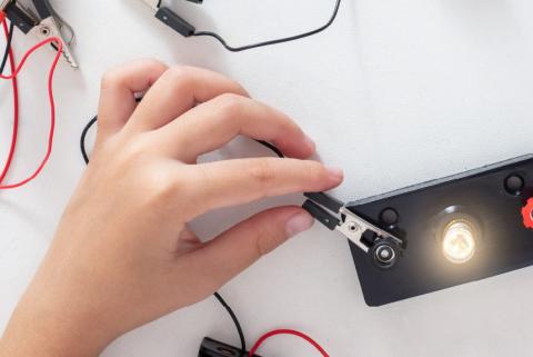 Child's hand manipulating alligator clips to generate electricity for a small light