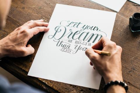 Man writing "Let your dreams be bigger than your fears" in a calligraphic style