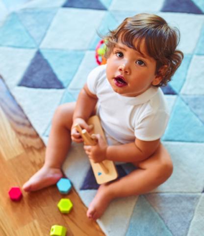 Infant sitting on blue blanket with toys, looking up at camera