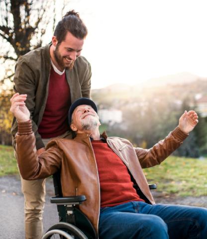 A young man pushed an elder man in a wheelchair, set outside