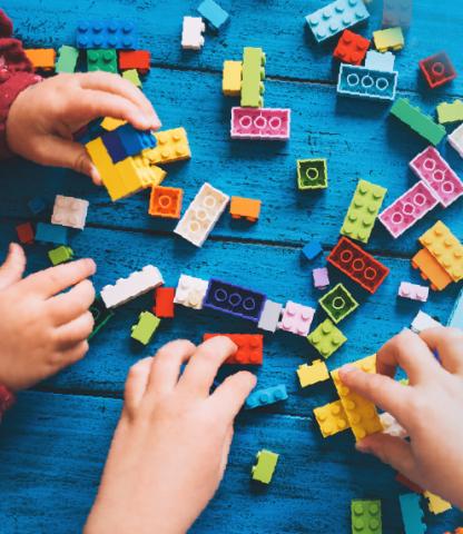 Two pairs of children's hands playing with Lego blocks