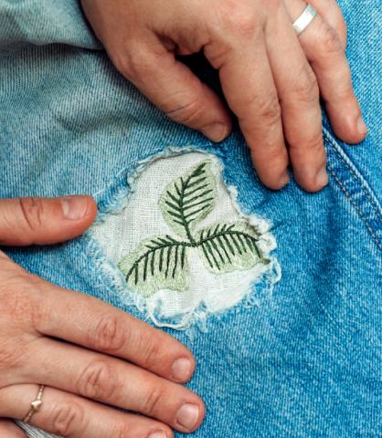 Image: Someone patching jeans. The patch has embroidered leaves on it.