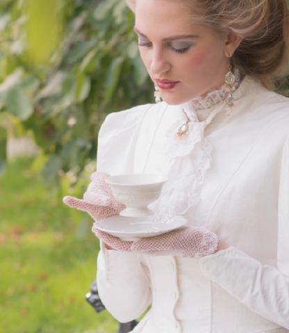 Young woman in Victorian dress holding a cup of tea while sitting outside
