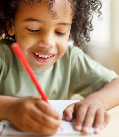 Child writing letter with red pen