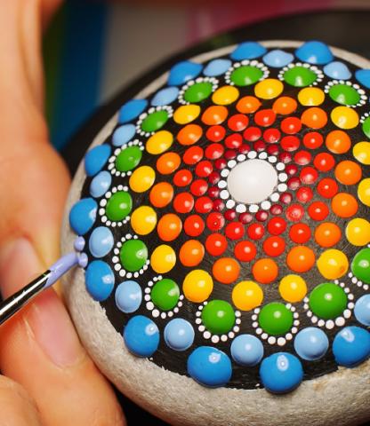 Person painting colorful mandala on rock