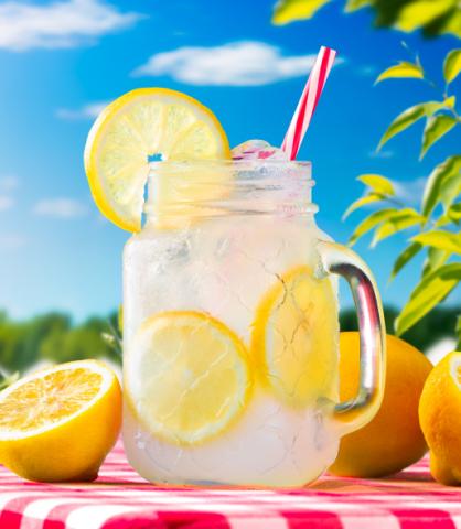 Mason jar of lemonade surrounded by lemons on a gingham table cloth