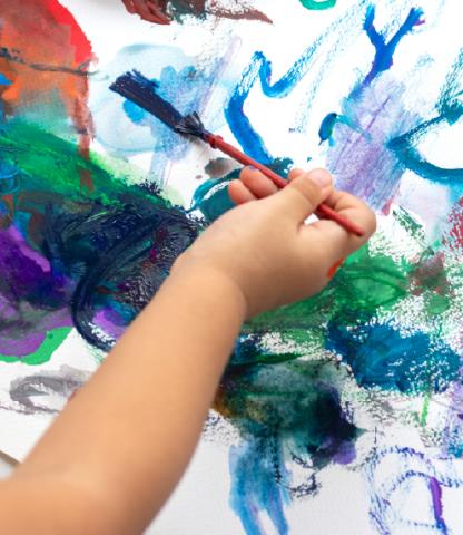 Young child holding paintbrush with abstract paint swipes on paper