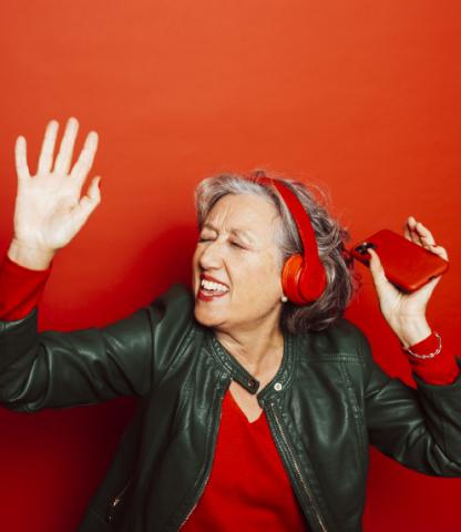 Senior woman dancing while wearing red headphones and holding a red cellphone