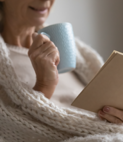 Woman drinking from cup with book and blanket