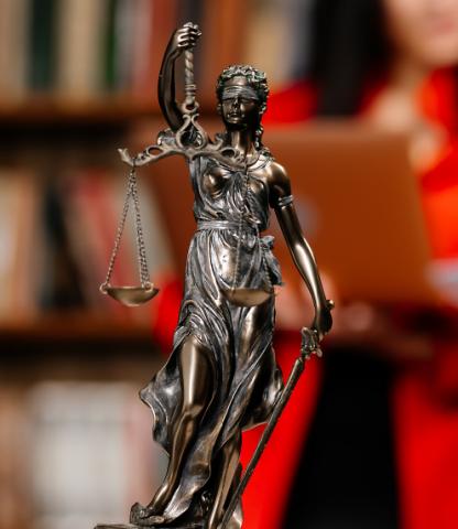 Lady Justice figure in bronze against blurred background of books