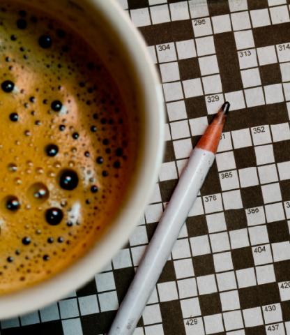 Overhead view of coffee in a cup, a pencil, and a blank crossword puzzle