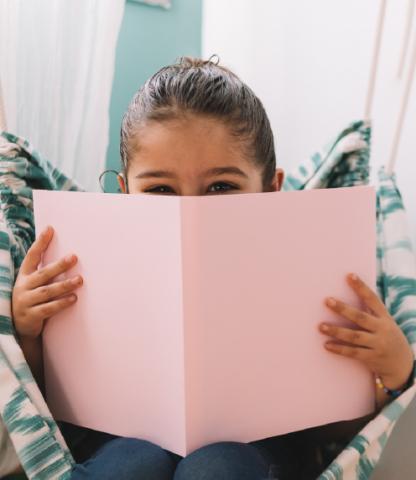 Young girl with face partially hidden by book