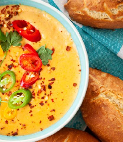 Cheese dip with slices of hot pepper on top and bread beside it