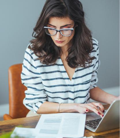 Woman working on a laptop, looking at paperwork next er