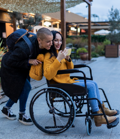 Woman in a wheelchair showing her phone to a woman standing behind her