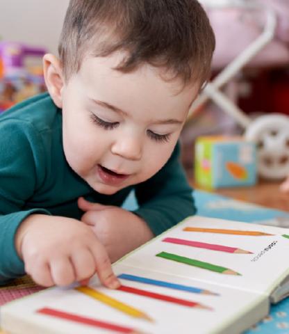 Young boy pointing out colored pencils in a book