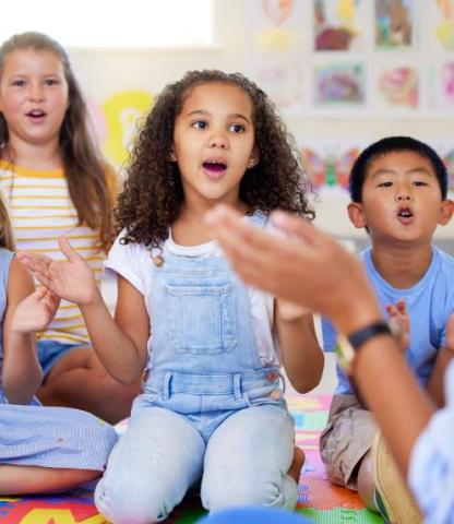 Three children singing while paying attention to an adult out of photo