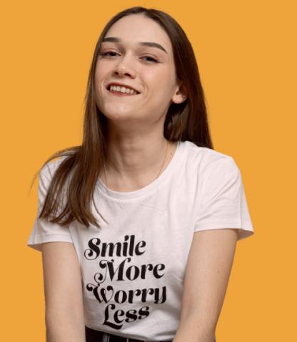 Young woman wearing a pink shirt with the text Smile More Worry Less in black letters on it
