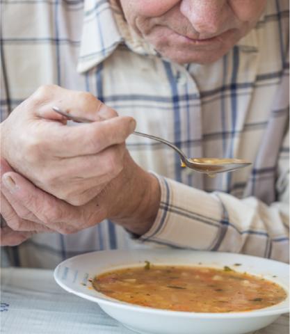 Elderly man holding his hand stand while he eats a bowl of soup