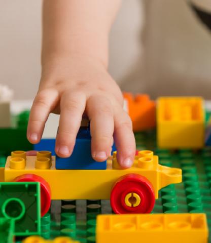 Toddler's hand holding a vehicle made of large Lego blocks