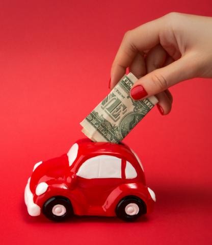 Woman placing dollar bills into a red car-shaped bank on a red background