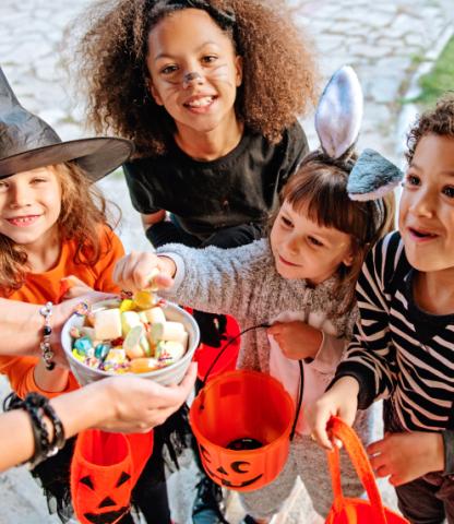 Image: A group of trick-or-treaters smiling and taking candy