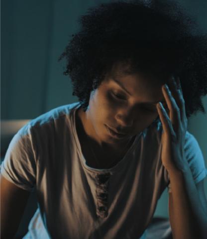 Woman in a dimly lit room, holding her head and looking uncomfortable