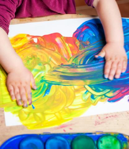 Child's hands smearing paint on a white sheet of paper