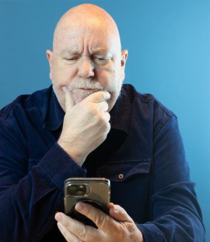 Mature man on blue background, starting contemplatively at his smartphone